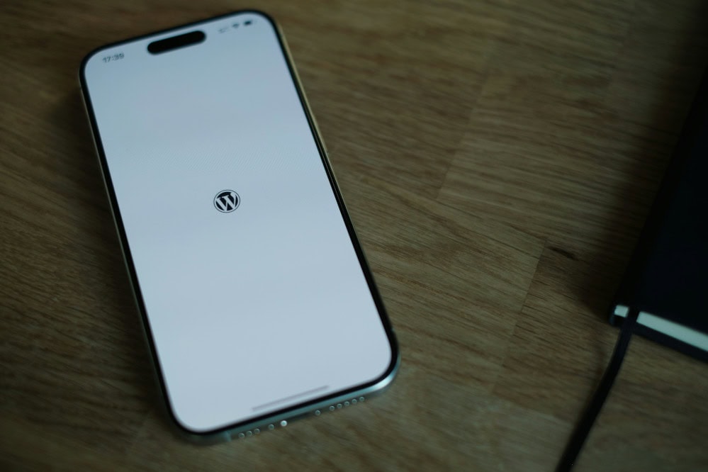 Smartfon z logo WordPress na białym tle, leżący na drewnianym stole.
