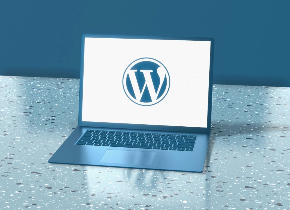 Laptop z logo WordPress na ekranie, ustawiony na białej powierzchni z dżetami.
